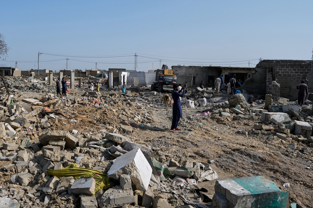 People walk through rubble as a hydraulic shovel demolish a structure during an operation against illegal settlement of Afghan refugees conducted by local government, on the outskirts of Karachi, Pakistan.