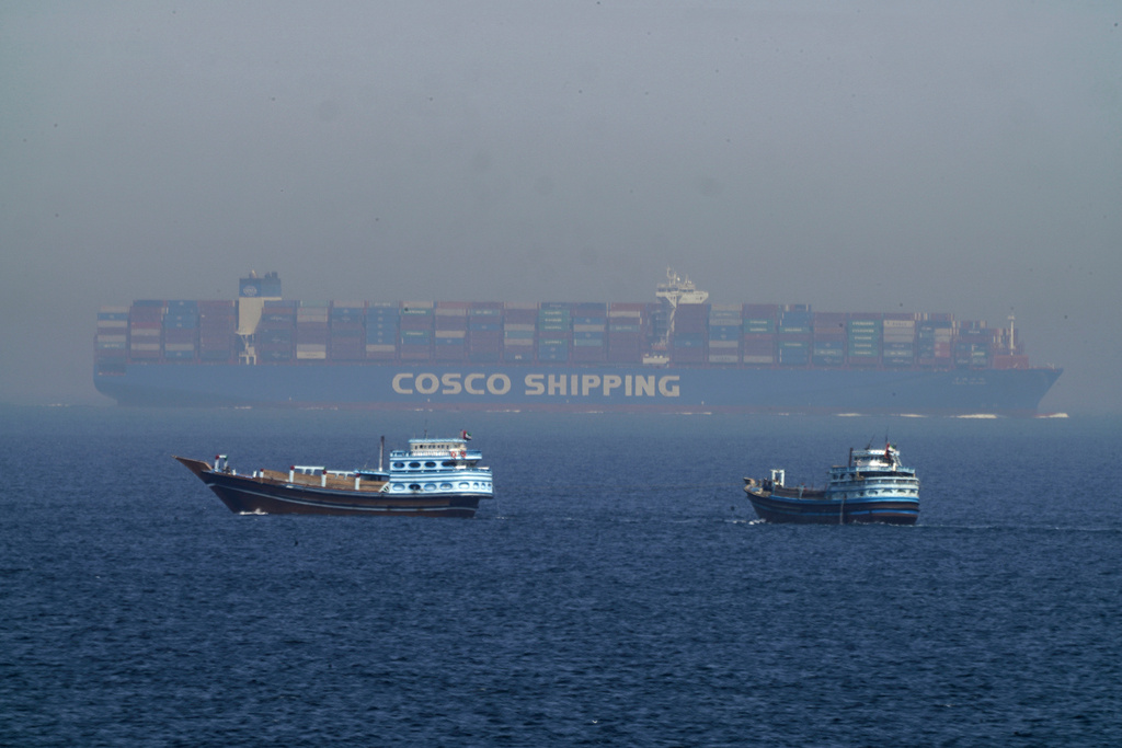 Two traditional dhows sail by a large container ship in the Strait of Hormuz.