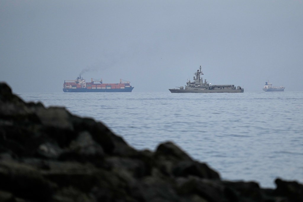A UAE navy ship sails next to a cargo ship in the Strait of Hormuz as seen from Khor Fakkan, United Arab Emirates, Wednesday, March 11, 2026.
