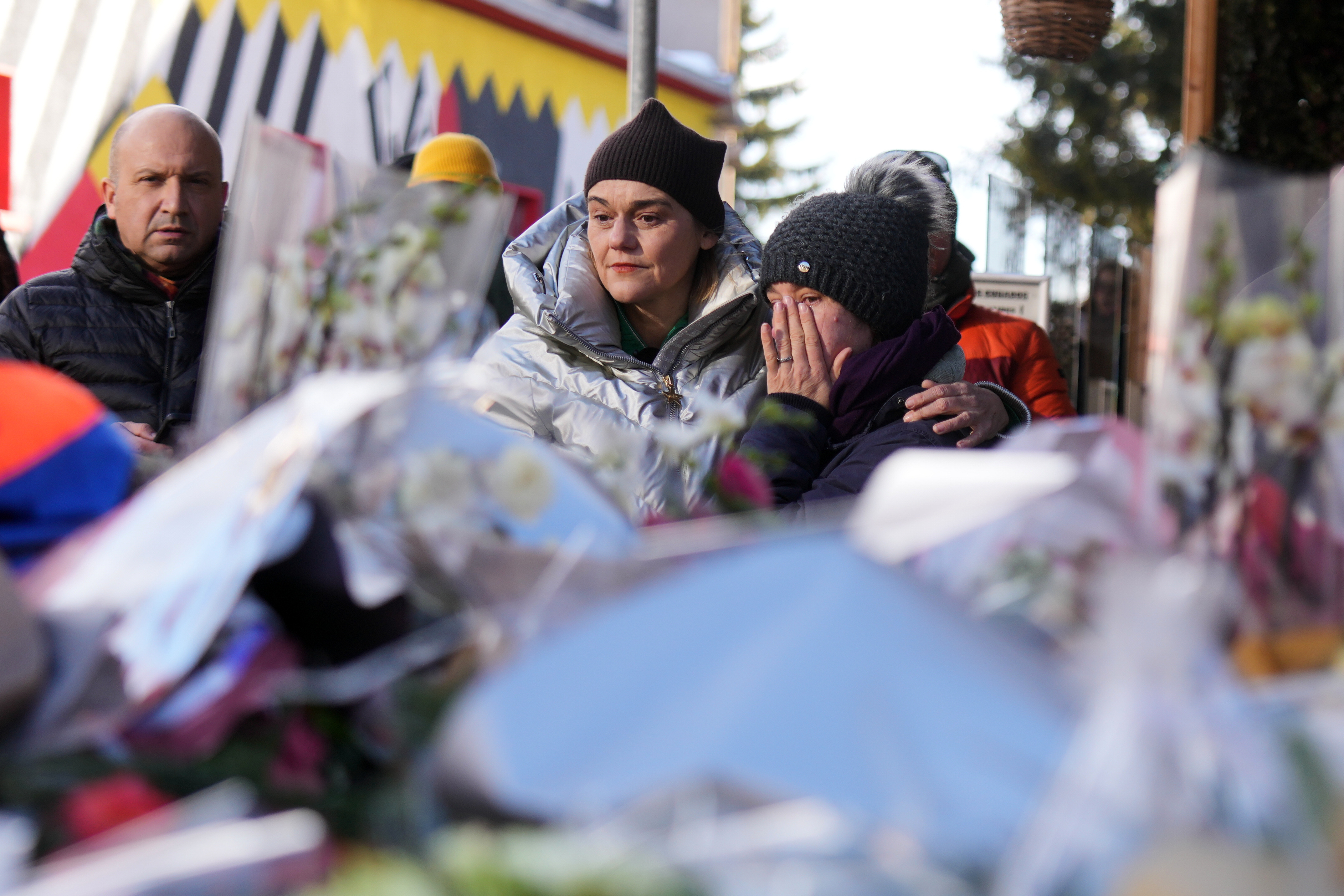People mourn behind flowers and letters near the sealed off Le Constellation bar, where a devastating fire left dead and injured during the New Year's celebrations in Crans-Montana, Swiss Alps, Switzerland, Friday, Jan. 2, 2026. 