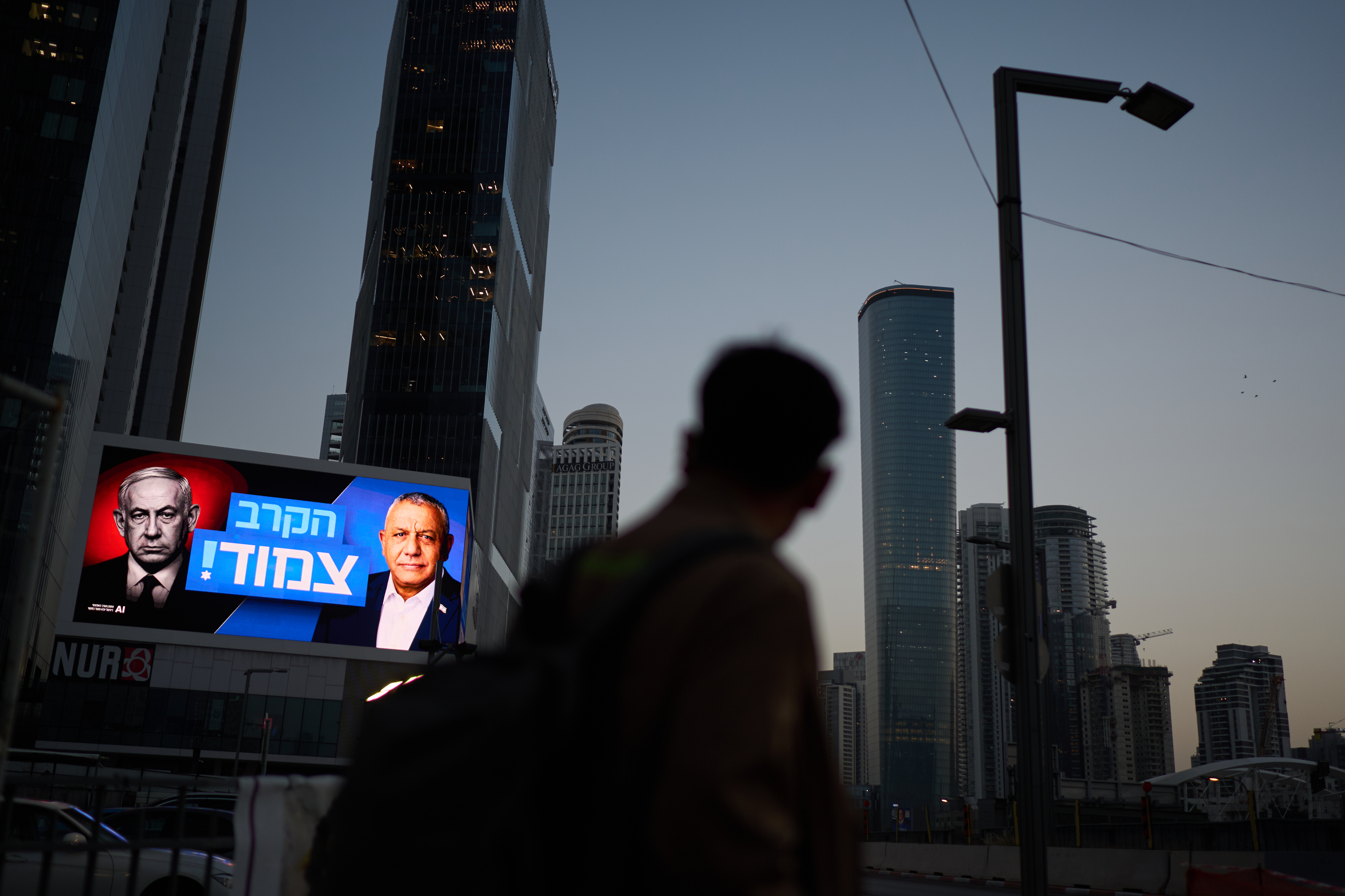 A pedestrian passes a campaign billboard featuring Israeli Prime Minister Benjamin Netanyahu, left, and his main rival, opposition candidate Gadi Eisenkot, with a message in Hebrew that reads "The race is tight," Friday, Oct. 23, 2026, in Tel Aviv, Israel.