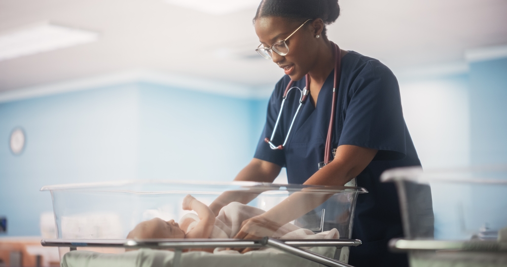Portrait of a Young Doctor Checking Up and Caring for a Newborn Baby Lying in a Bassinet in a Modern Maternity Ward.