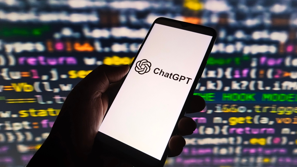 ChatGPT AI logo displayed on smartphone screen, with colorful computer code in background, symbolizing AI technology and programming.