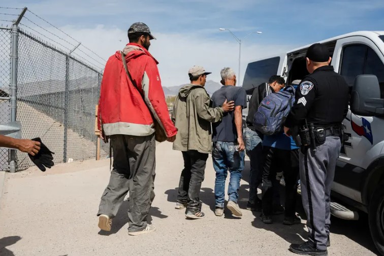 A group of migrants walk to an El Paso County Sheriff transport van to be taken to processing on March 20, 2024. State troopers have responded to efforts by migrants to rush through border gates en masse by charging hundreds of migrants with rioting. 