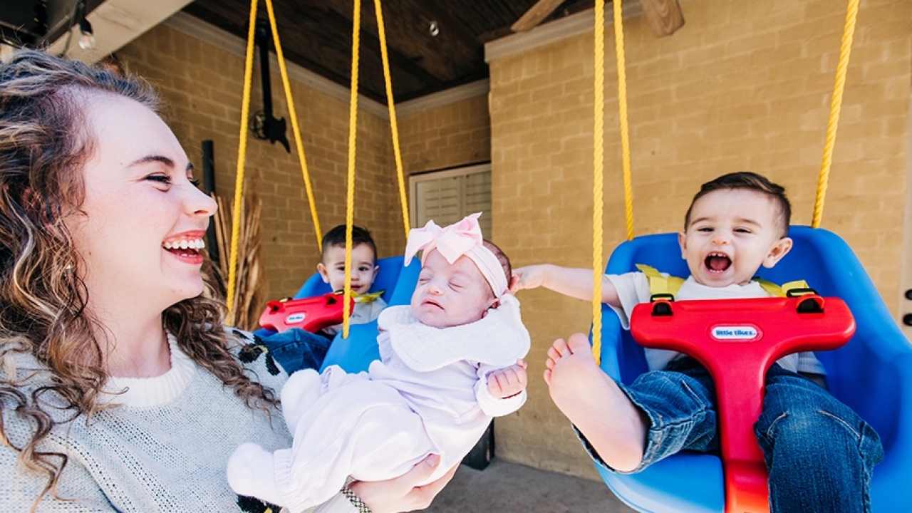 Britney Alba holds one of her twin girls, while her twin boys swing.