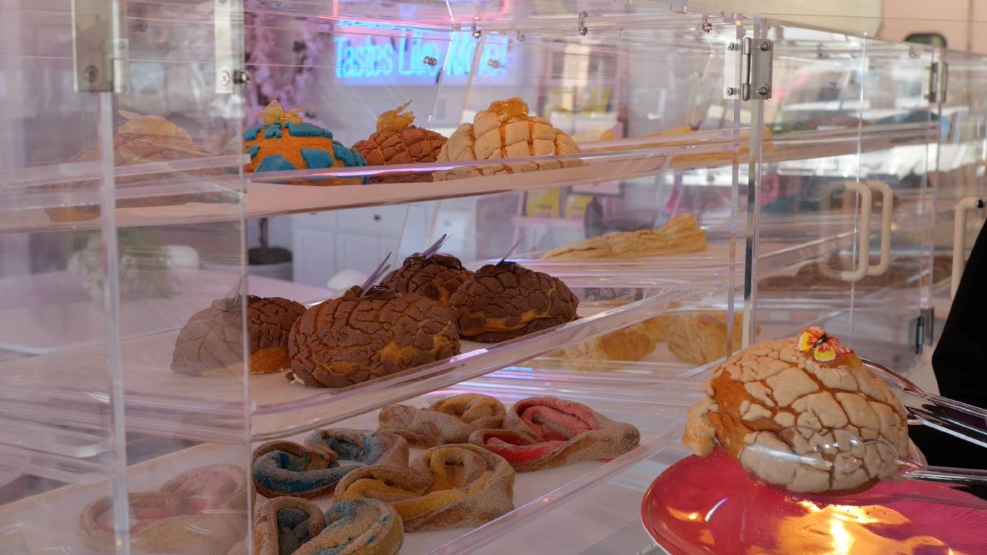 The pan dulce [sweet bread] and other pastries are placed in acrylic display cases; guests use tongs to get their sweet treat. Featured in the image is a ‘specialty concha.’