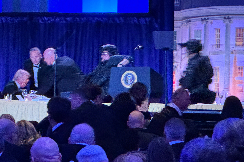 President Donald Trump, left, is seated on stage as U.S. Secret Service agents respond to take him from the ballroom after a shooting incident outside the ballroom during the White House Correspondents Dinner, Saturday, April 25, 2026, in Washington. 