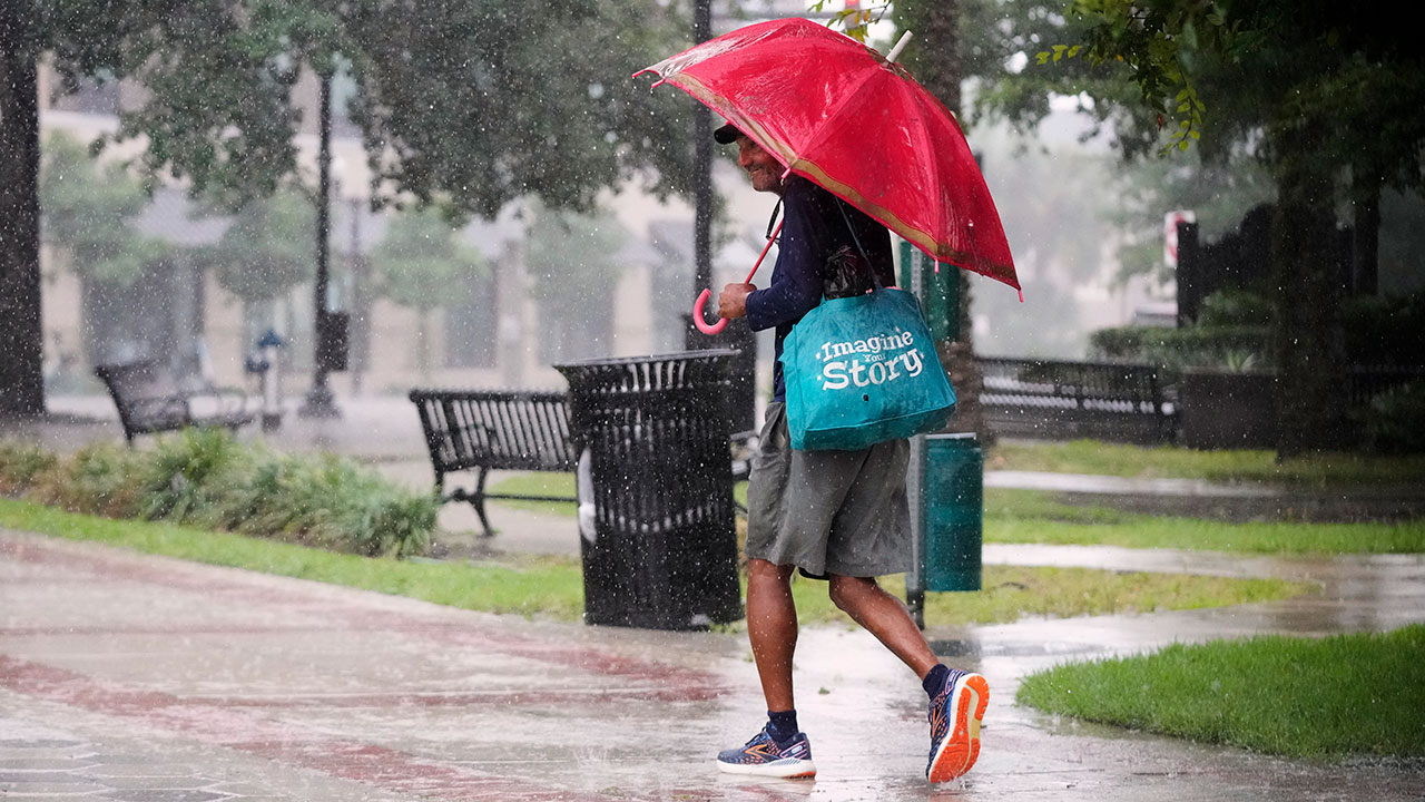 A pedestrian walks along a street during a rain shower Tuesday, July 15, 2025, in Orlando, Fla., as tropical weather moves over the state.