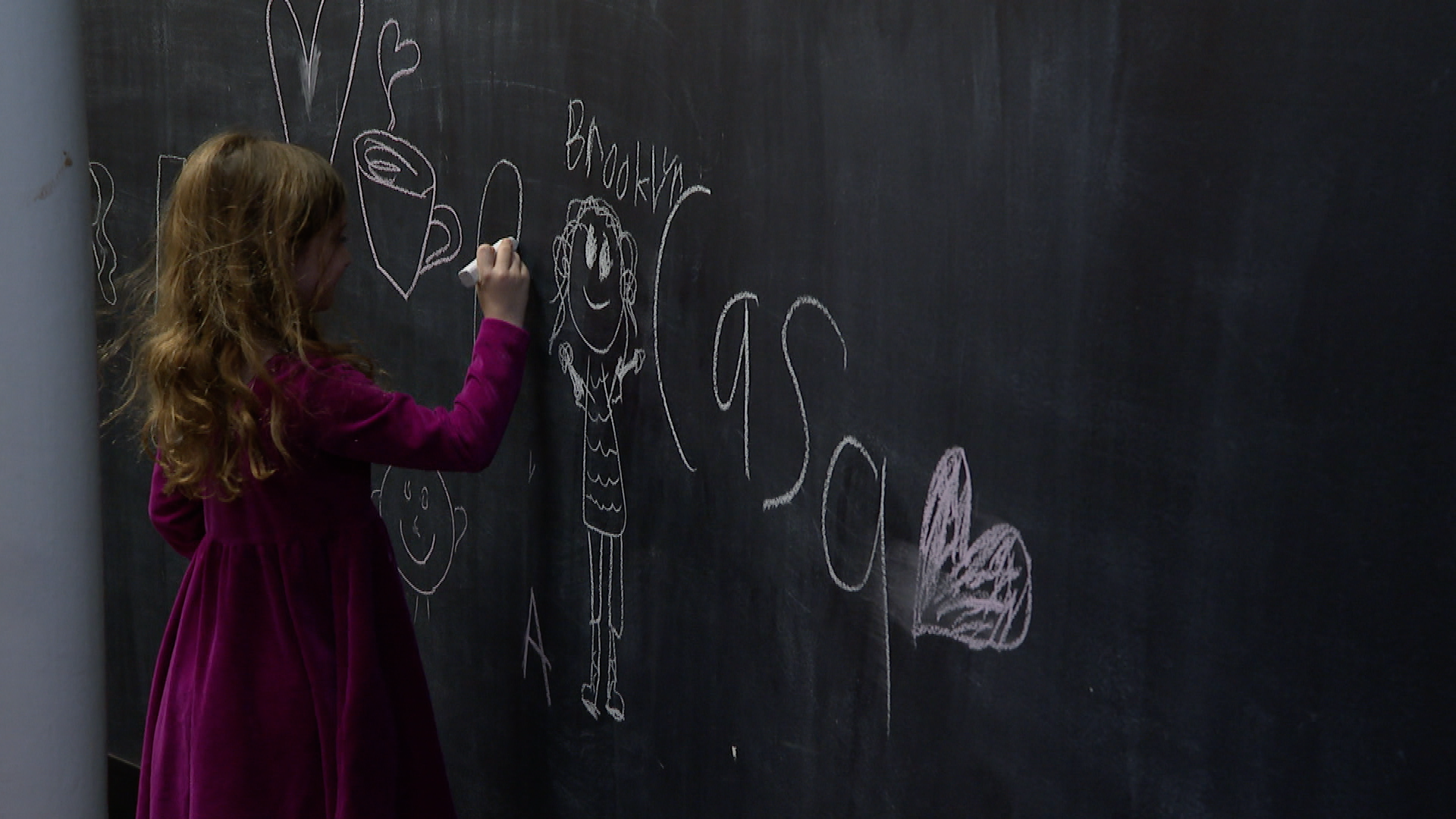 A little girl draws on a chalkboard