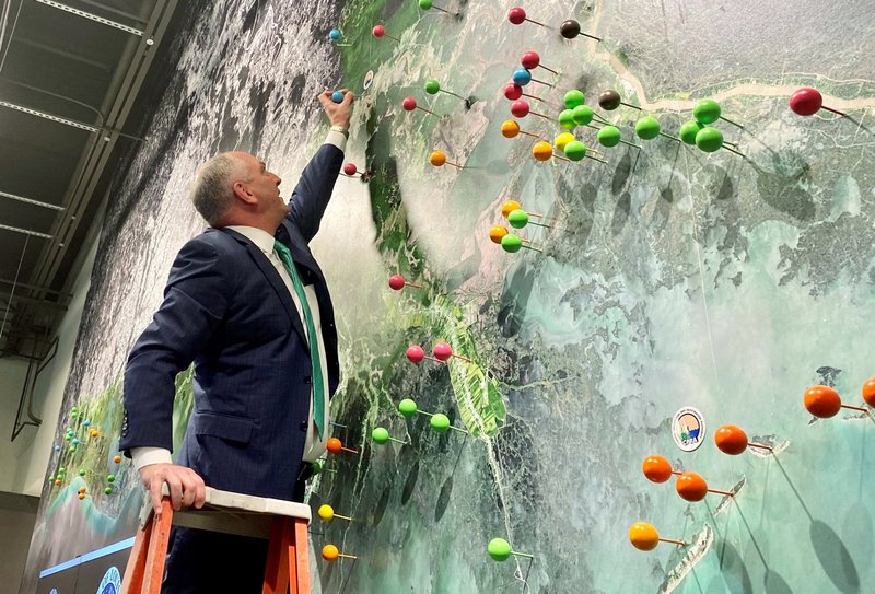 In this photo provided by the Coastal Protection and Restoration Authority, Louisiana Gov. John Bel Edwards sticking a large pin in a mural of Louisiana's coast, in Baton Rouge, La., Wednesday, Feb. 12, 2020, to show the location of the Maurepas Swamp. A council created to allocate money from water pollution fines paid after the catastrophic BP oil spill voted Wednesday to give Louisiana $130 million to link the state's second-largest coastal swamp back up to the Mississippi River, providing fresh water and sediment to nourish it. (Coastal Protection and Restoration Authority via AP)