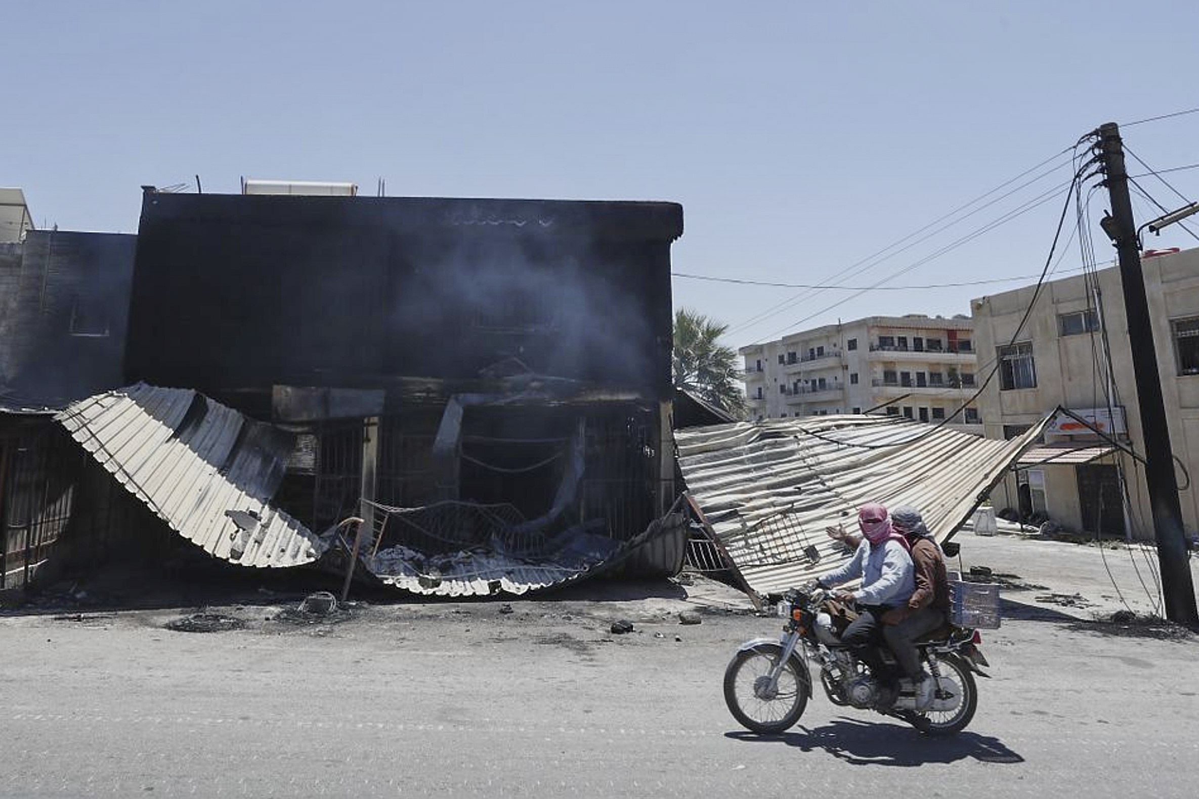 Syrian citizens ride in front of a shop that was burned during clashes between Syrian government forces and Druze militias on the outskirts of Sweida city, southern Syria, Wednesday, July 16, 2025.