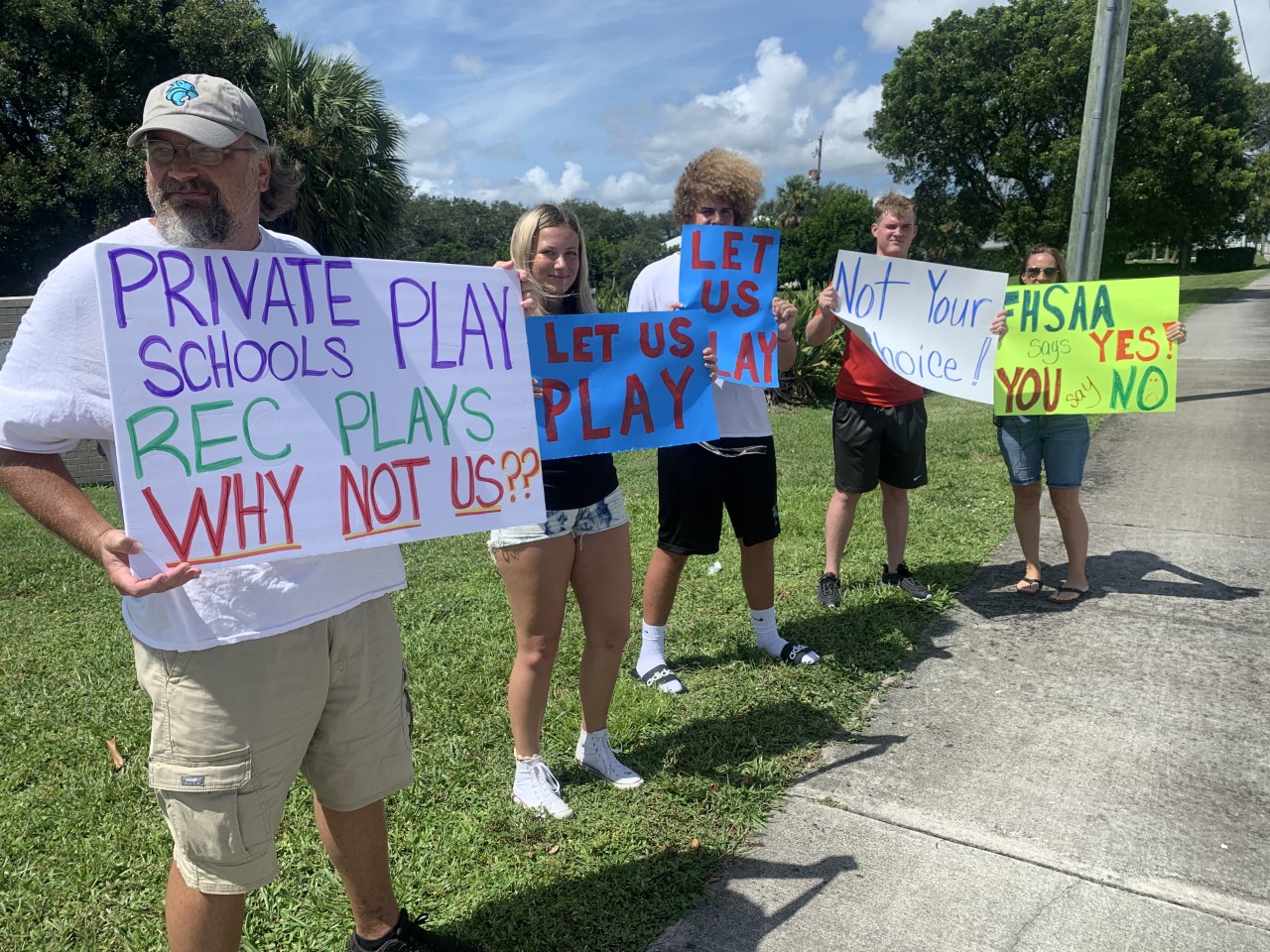 Parents and student-athletes hold signs in protest of sports not being played