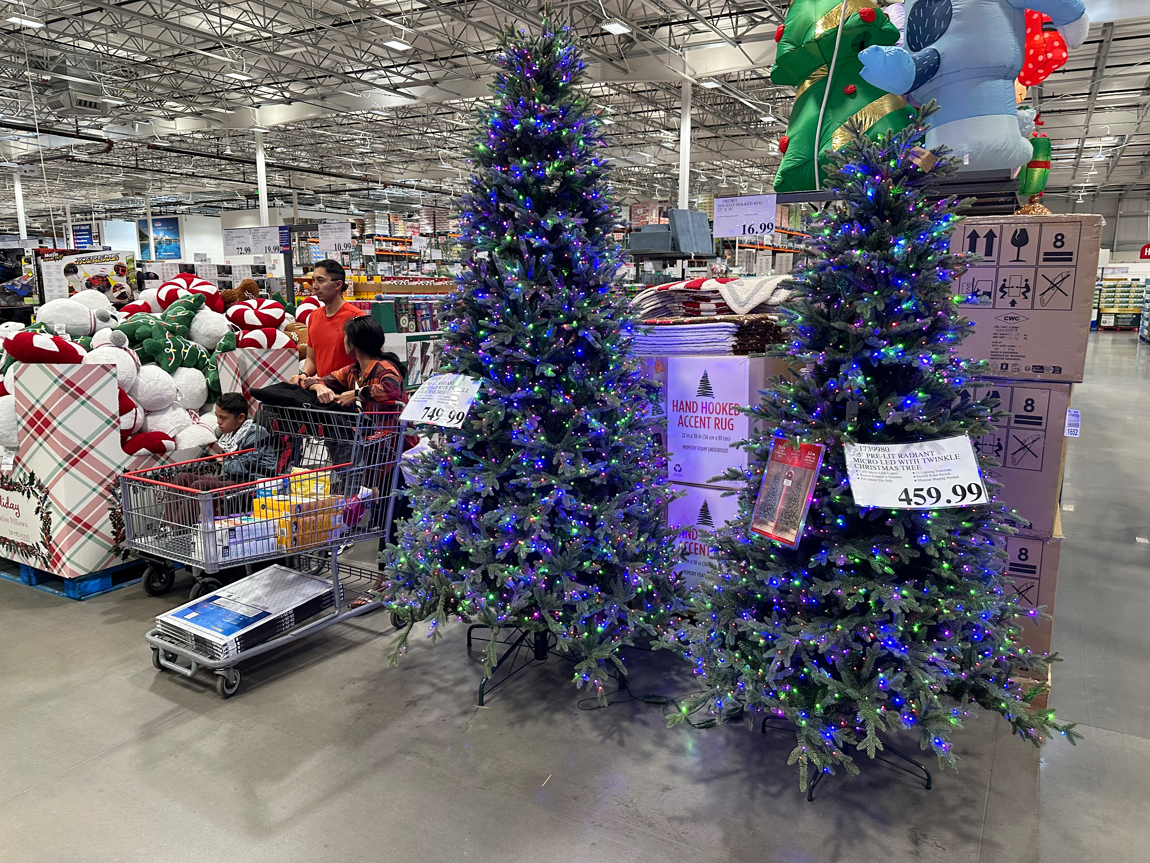 Shoppers pass by holiday trees on display in a Costco warehouse.