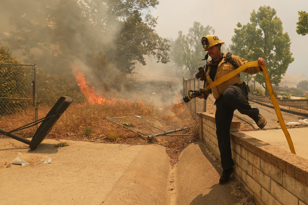 A firefighter hops over a fence while battling the Sandy Fire Monday, May 18, 2026, in Simi Valley, Calif. 