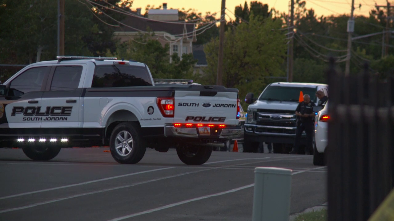 A still from the scene shot by a FOX 13 Photojournalist. It's evening, and the street is blocked off by a pickup truck with South Jordan Police branding.