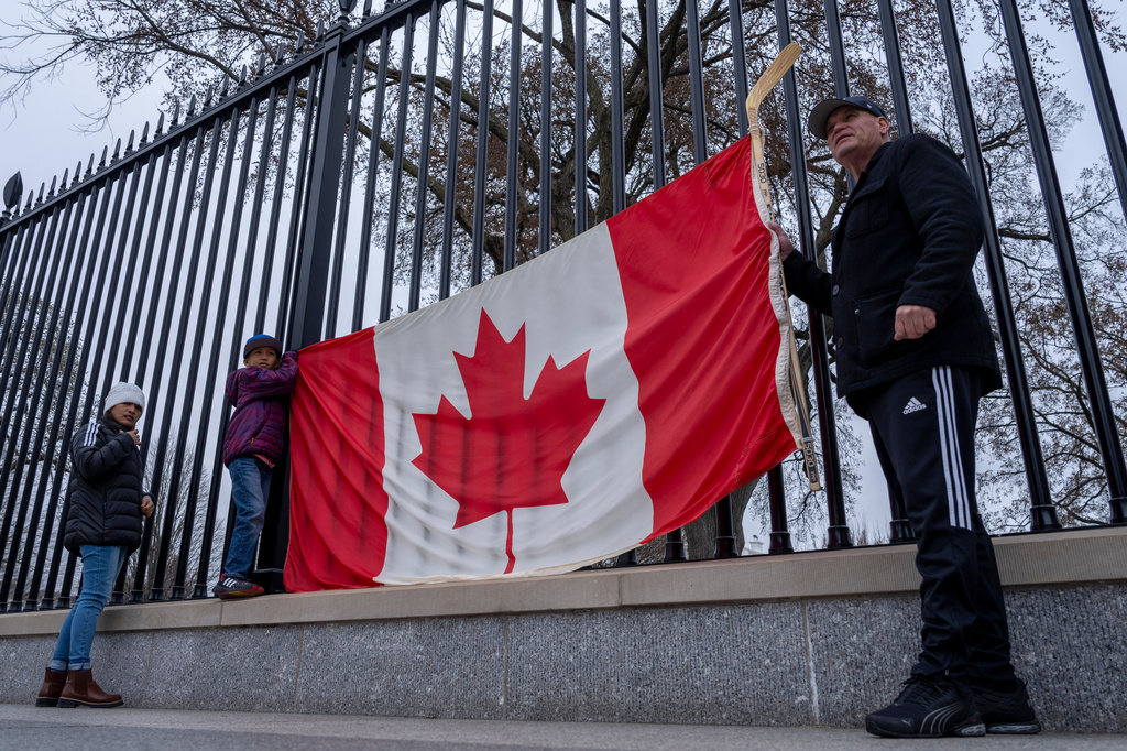 FILE - From right, Toronto residents Douglas Bloomfield, his son Phoenix and wife Ame, who are on vacation in Washington, hold a Canadian flag and an ice hockey stick to show their support for Canada regarding trade tariffs, in front of the White House in Washington, March 13, 2025. 
