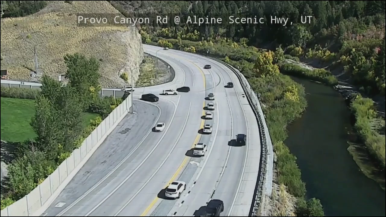 A snapshot from a UDOT traffic camera showing a section of the Alpine Loop. It's daytime. A line of cars sits in the left turn lane, hoping to turn off.