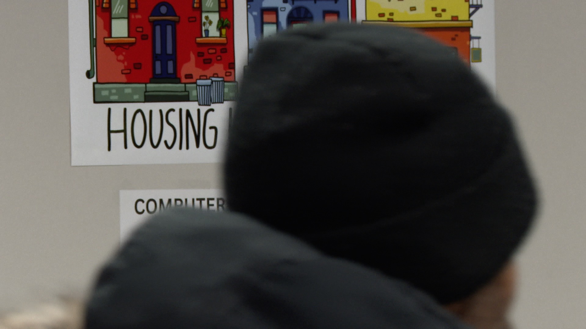 Man inside Punks With Lunch building walks past 'Housing is a Human Right' sign