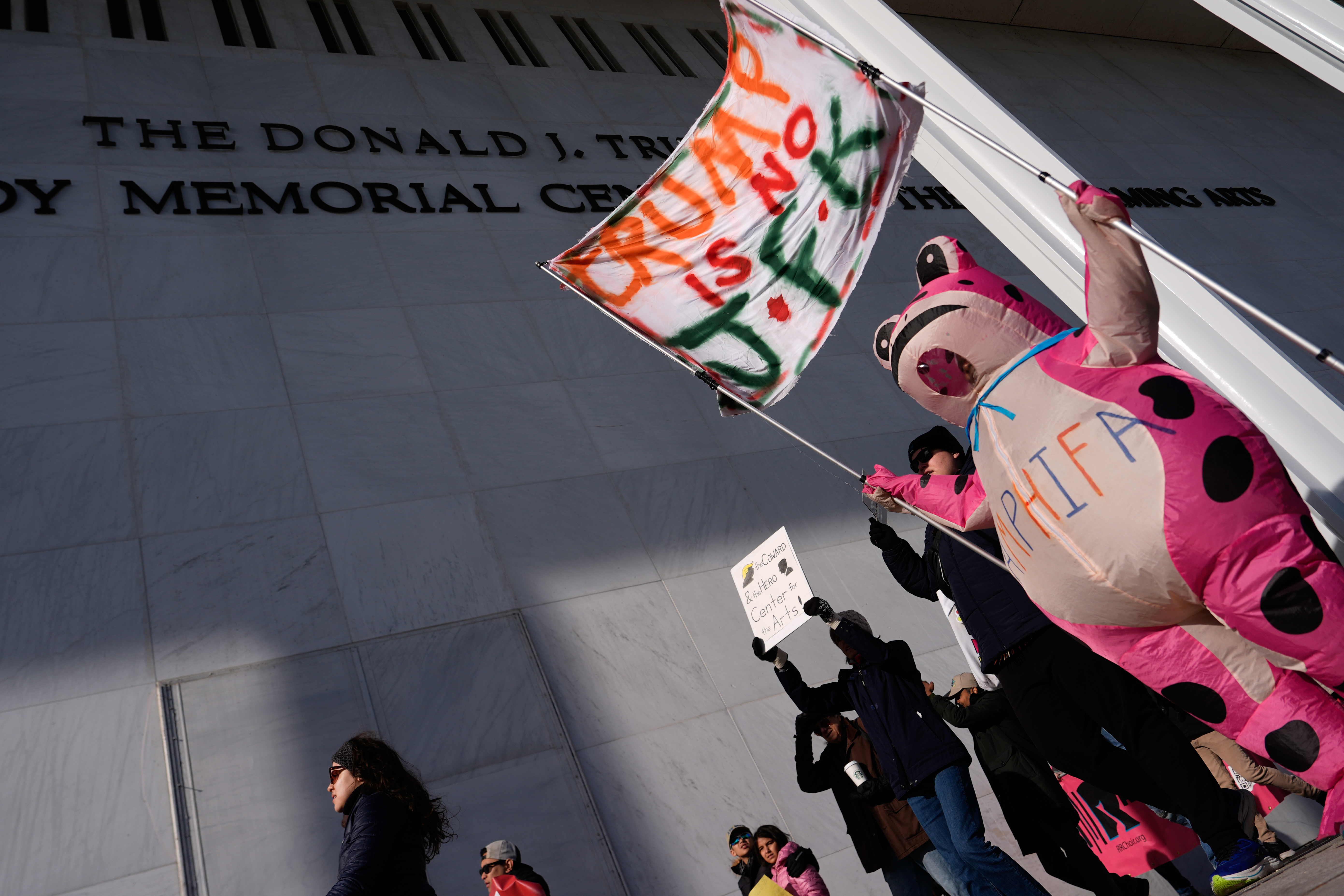 Demonstrators, including Nadine Siler, of Waldorf, Md., dressed in a pink frog costume, protest at the John F. Kennedy Memorial Center for the Performing Arts, a day after a Trump-appointed board voted to add President Donald Trump's name to the Kennedy Center, Saturday, Dec. 20, 2025, in Washington.