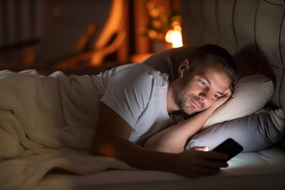 Man lying in bed looking at a cellphone.