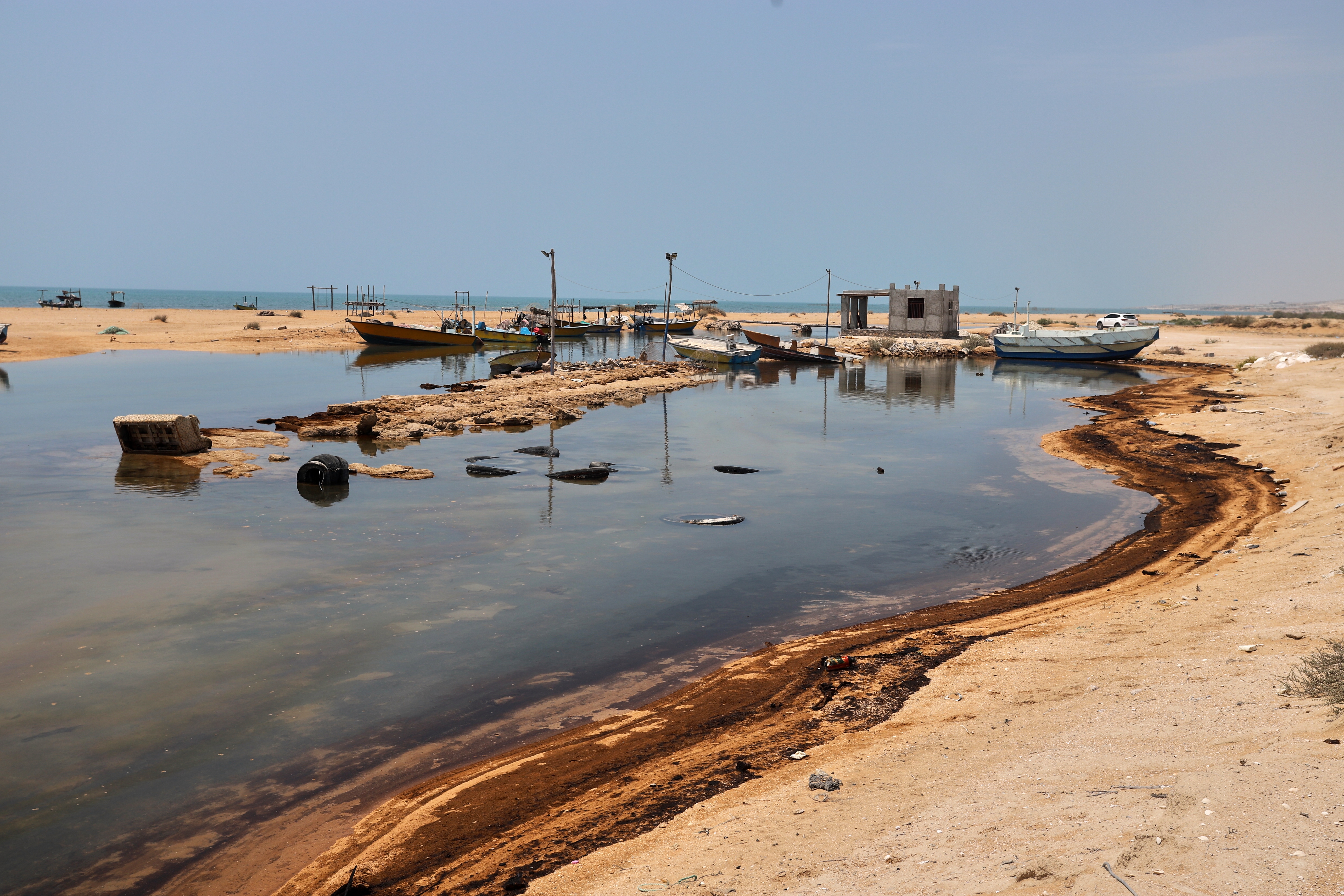 Oil residue lines the shore near fishing boats on Qeshm Island, Iran, Thursday, Aug. 13, 2026, amid ongoing wartime attacks on vessels and infrastructure in and around the Strait of Hormuz, though the spill's source has not been independently determined.