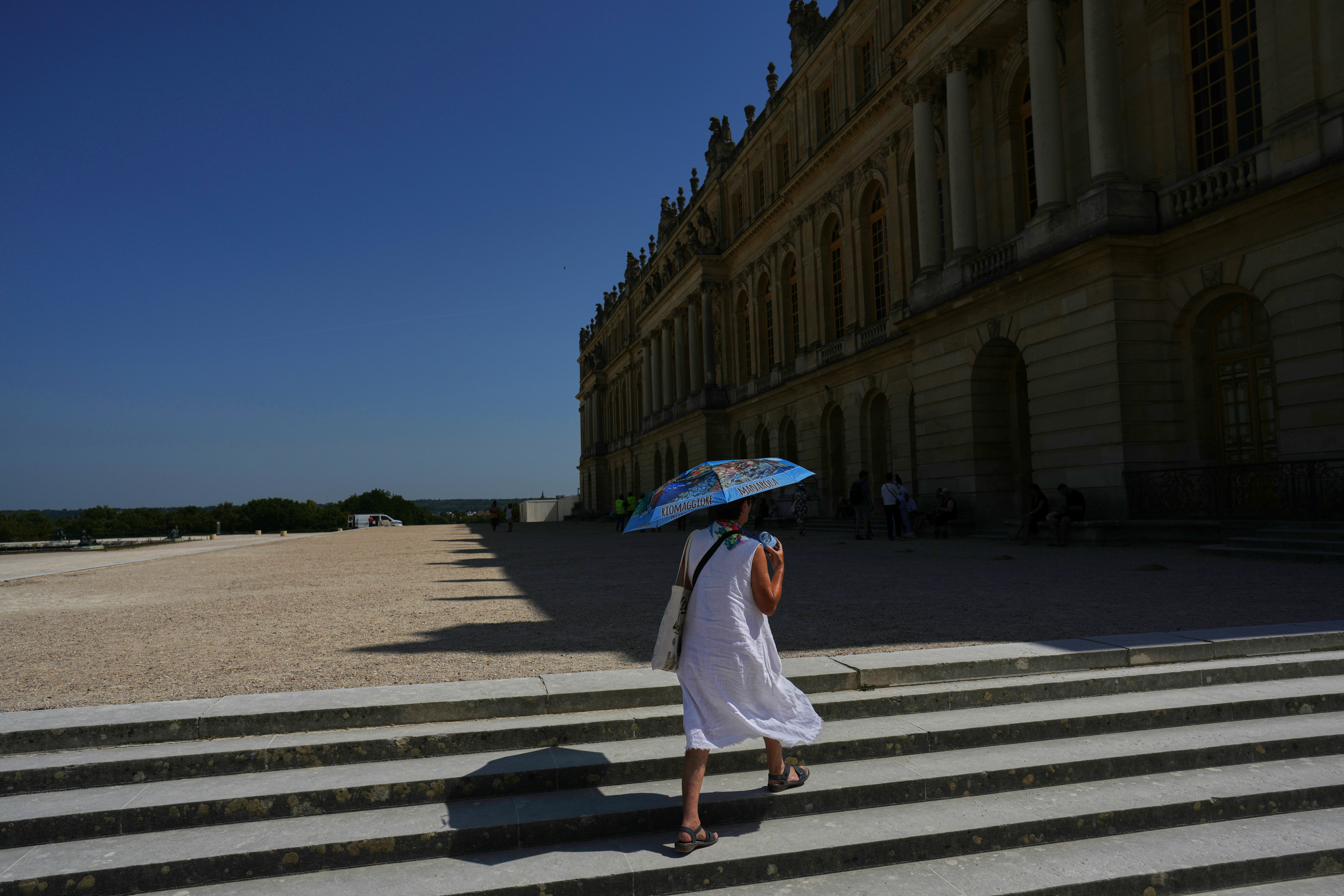 A woman shields herself from the sun with an umbrella as she walks in the garden of the Palace of Versailles, outside Paris, Monday, June 22, 2026.