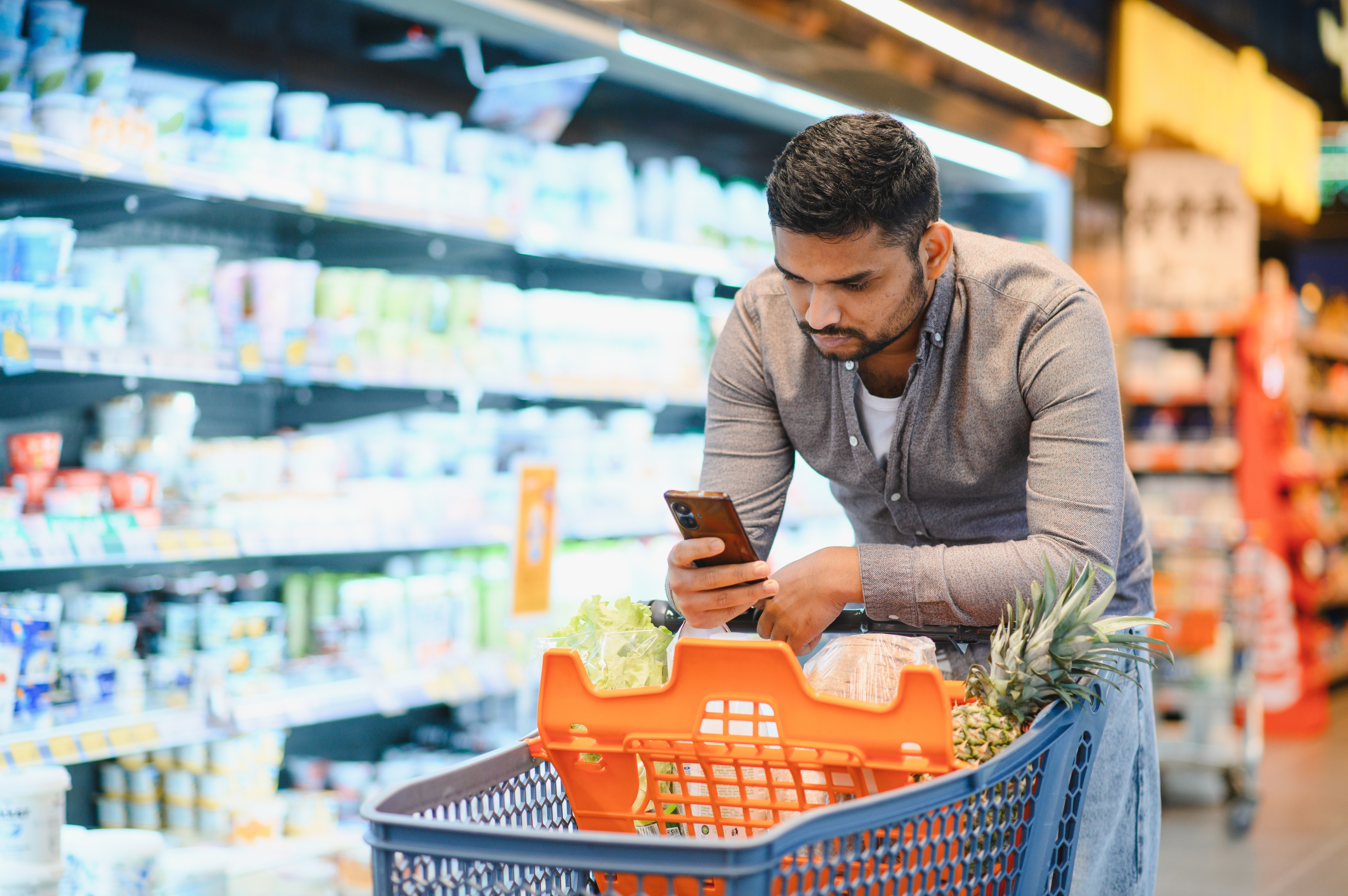 A man checks his phone while shopping for groceries. 