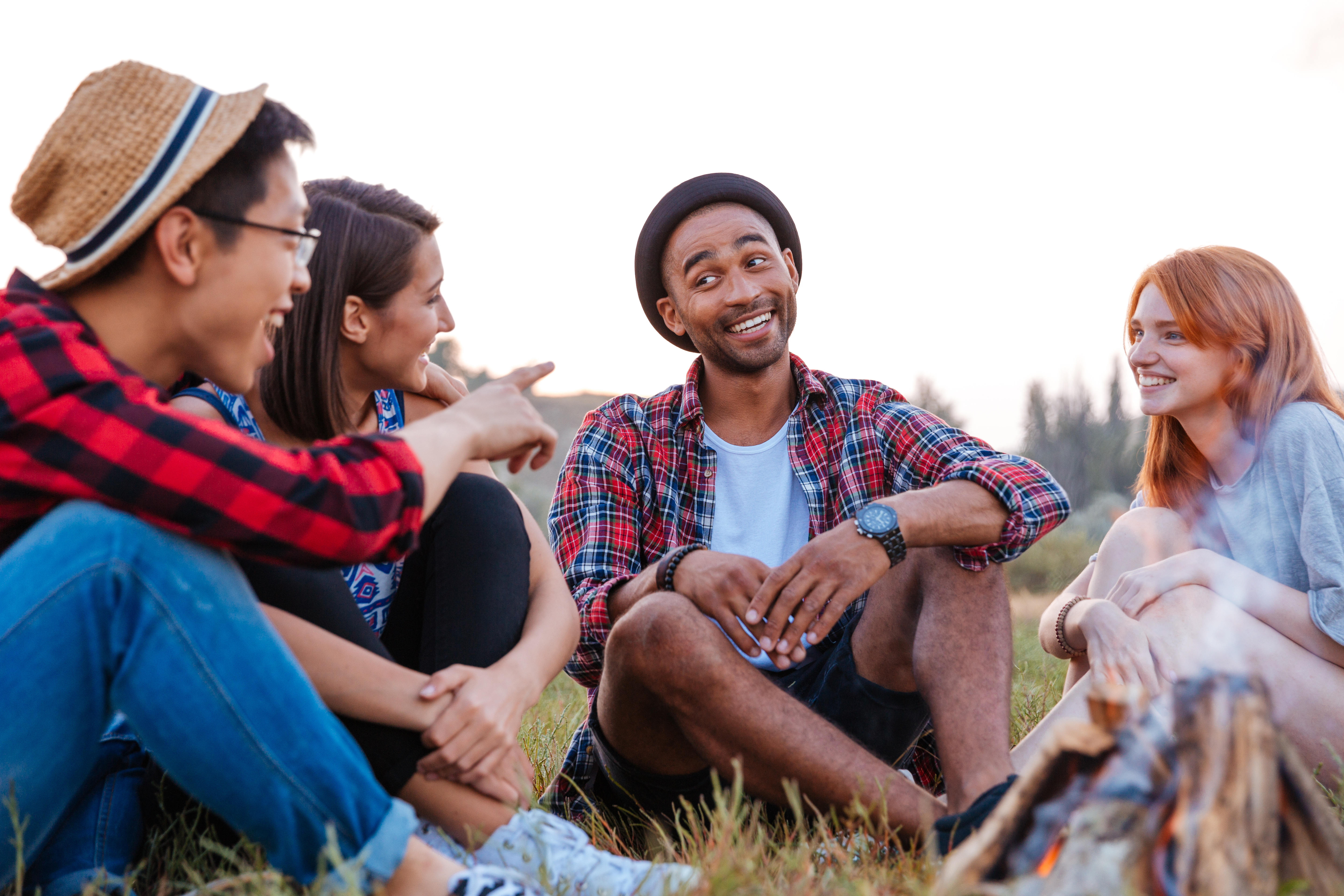 Smiling young people sitting and talking near bonfire