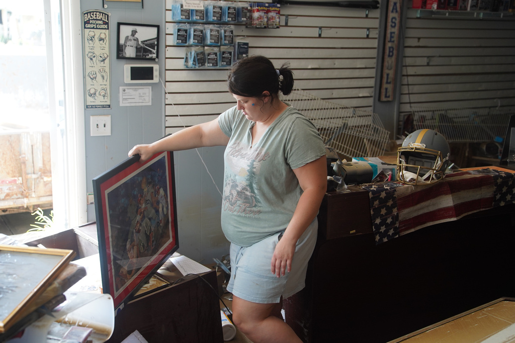 Kaylyn Boyd carries a framed photograph from her father's flooded sports card shop in Cambridge City, Ind., Thursday, Aug. 13, 2026. 