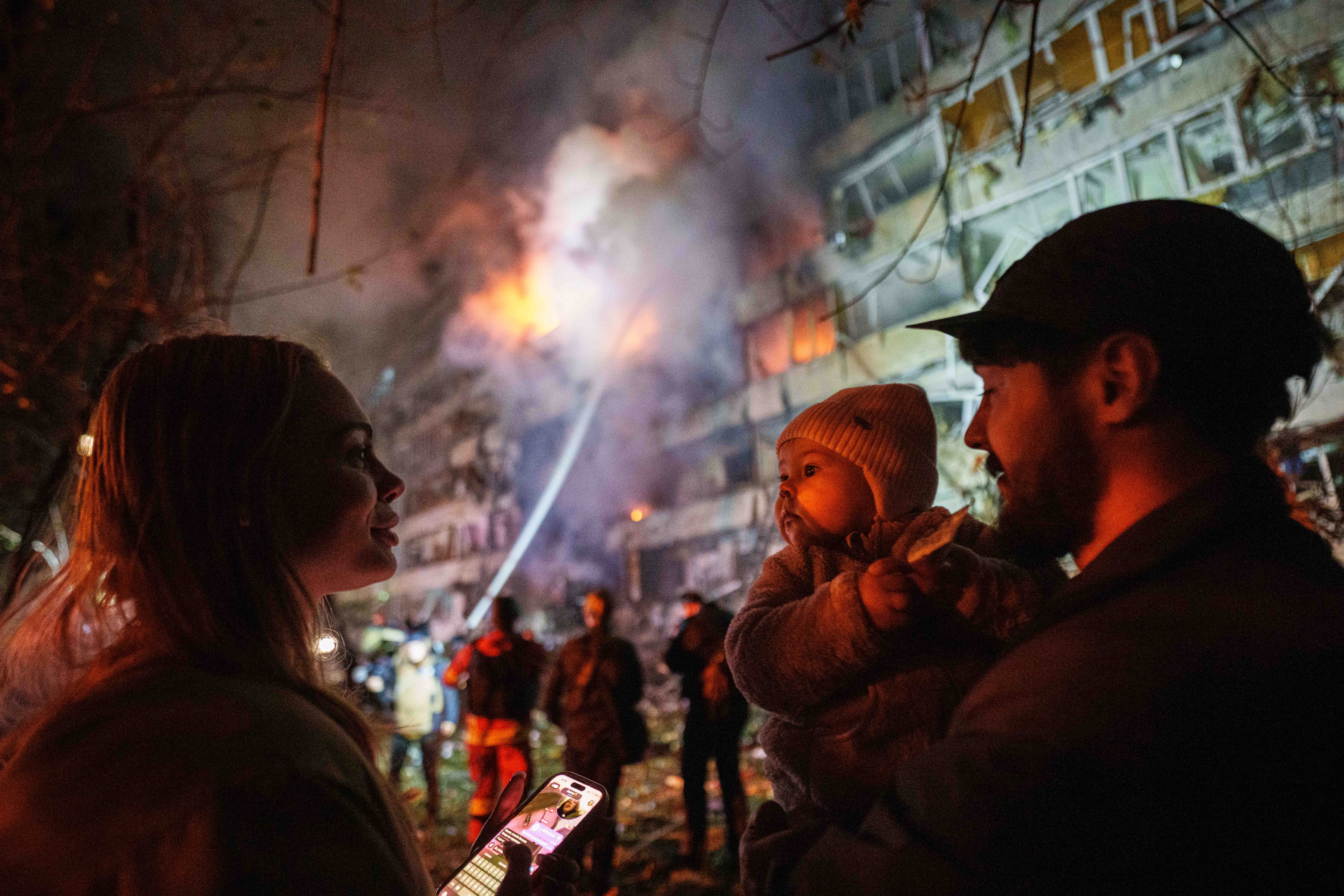 Victoria Deineko, her husband Ievhen Deineko and their daughter Mia look at a multi-story residential building damaged in a Russian missile strike in Kyiv, Ukraine, Tuesday, Oct. 13, 2026.