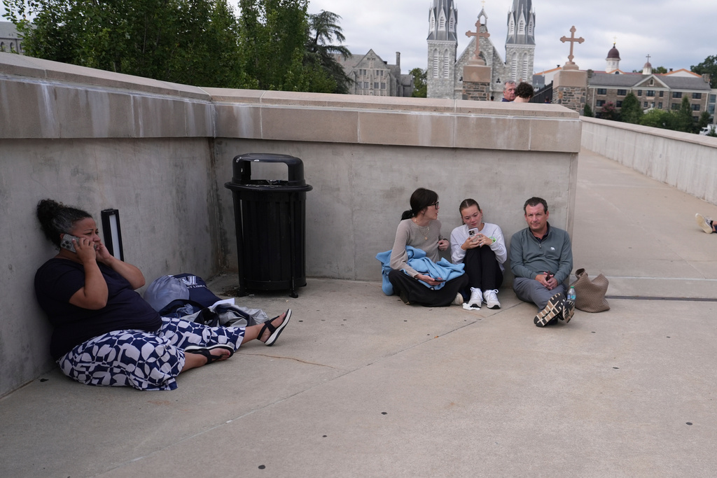 People shelter behind a wall on the Villanova University campus in Villanova, Pa., on Thursday, Aug. 21, 2025, where an active shooter was reported.