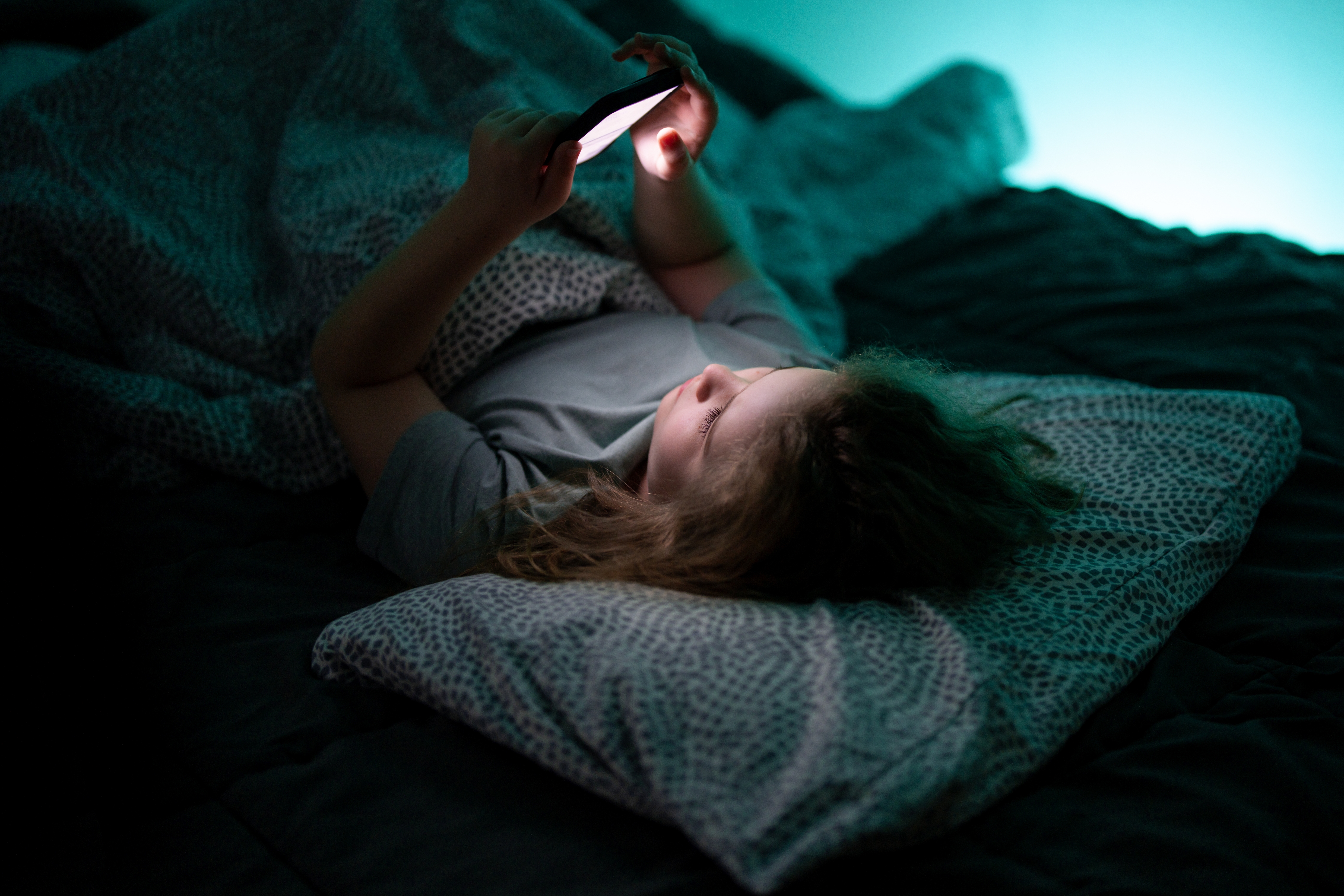 Teen watching media on their phone in a bed.