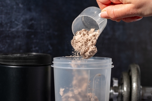 Stock image of a person dumping protein powder into a cup.