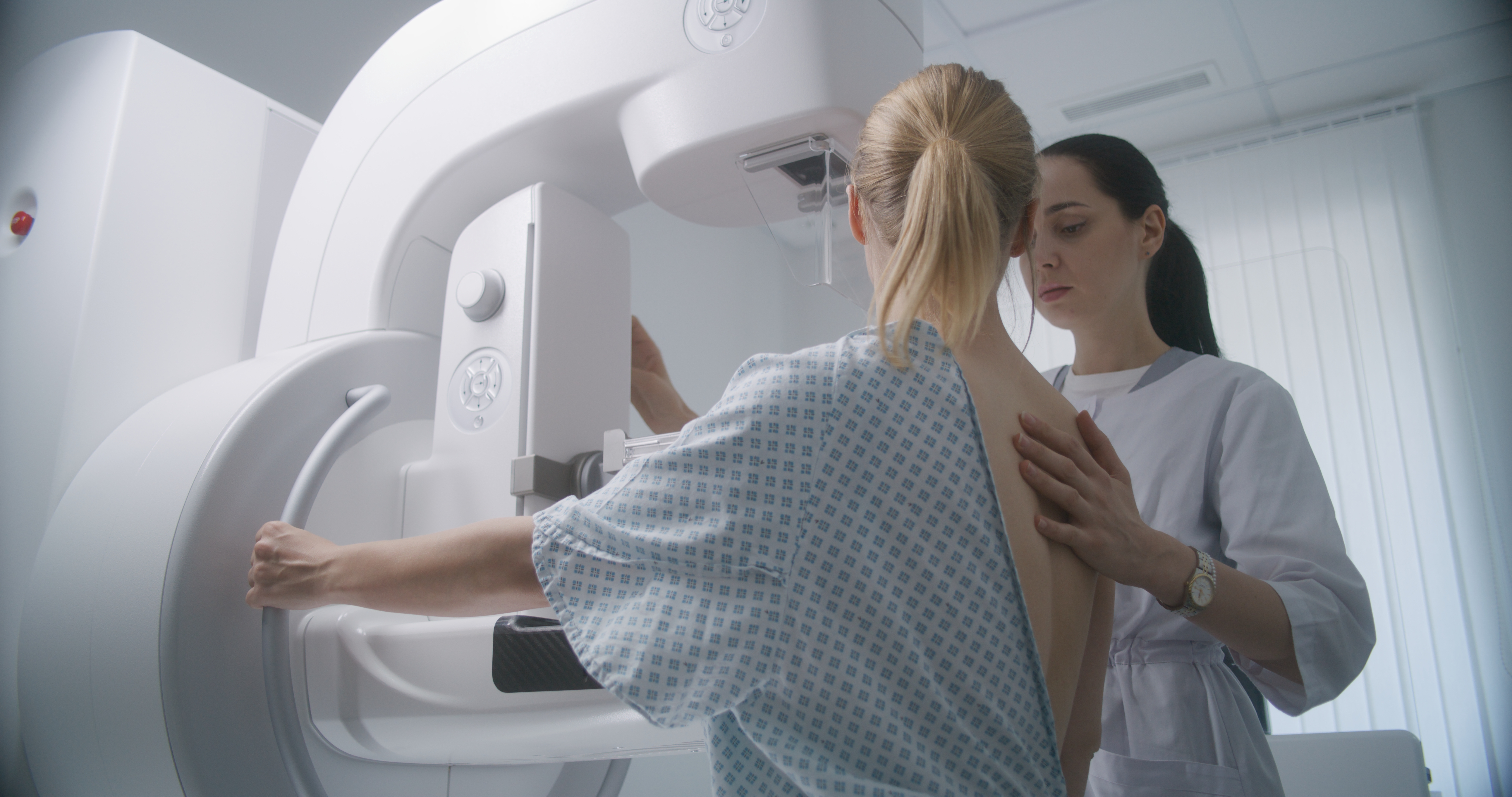Doctor adjusts modern mammogram machine for patient, uses computer.