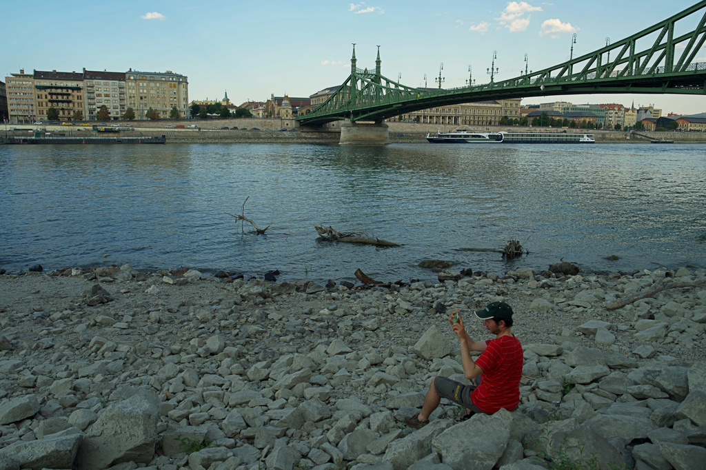 A man takes pictures as he sits on the dry bank of the Danube river in downtown Budapest, Hungary, Wednesday Aug. 5, 2026, as the river, which runs through 10 European countries, has receded never-before-seen low water levels. 