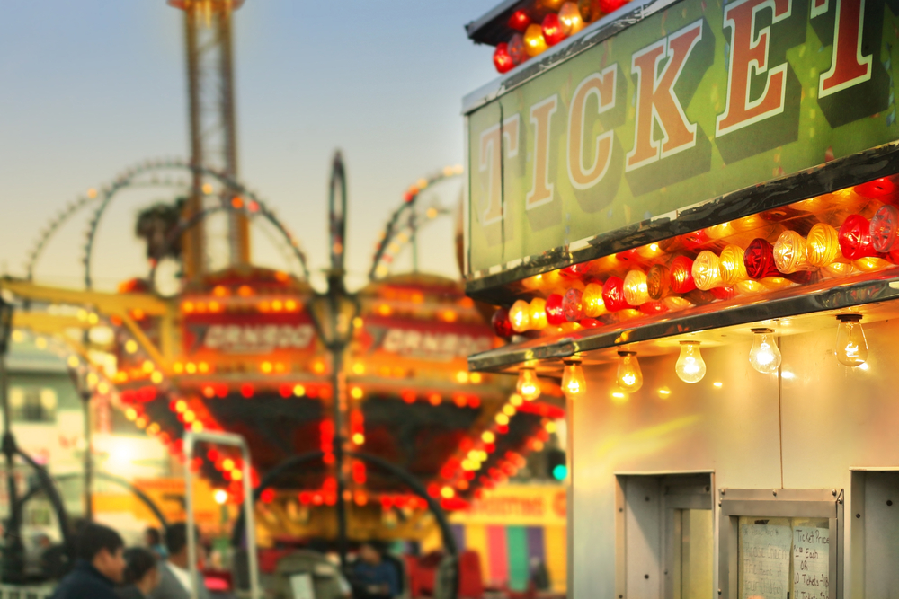 scene at a classic carnival with a ticket booth in the foreground (focal point on the ticket sign) with overall subtle retro vintage tone and styling