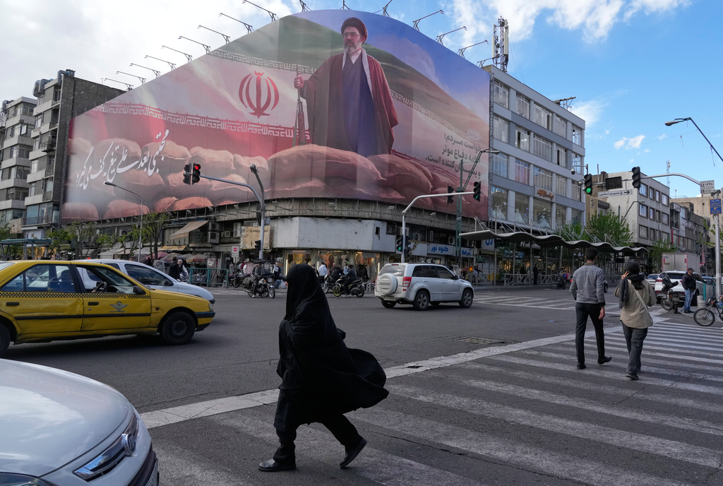People walk past a billboard that shows a graphic depicting Iran's Supreme Leader Ayatollah Mojtaba Khamenei in downtown Tehran, Iran, Monday, April 6, 2026. 