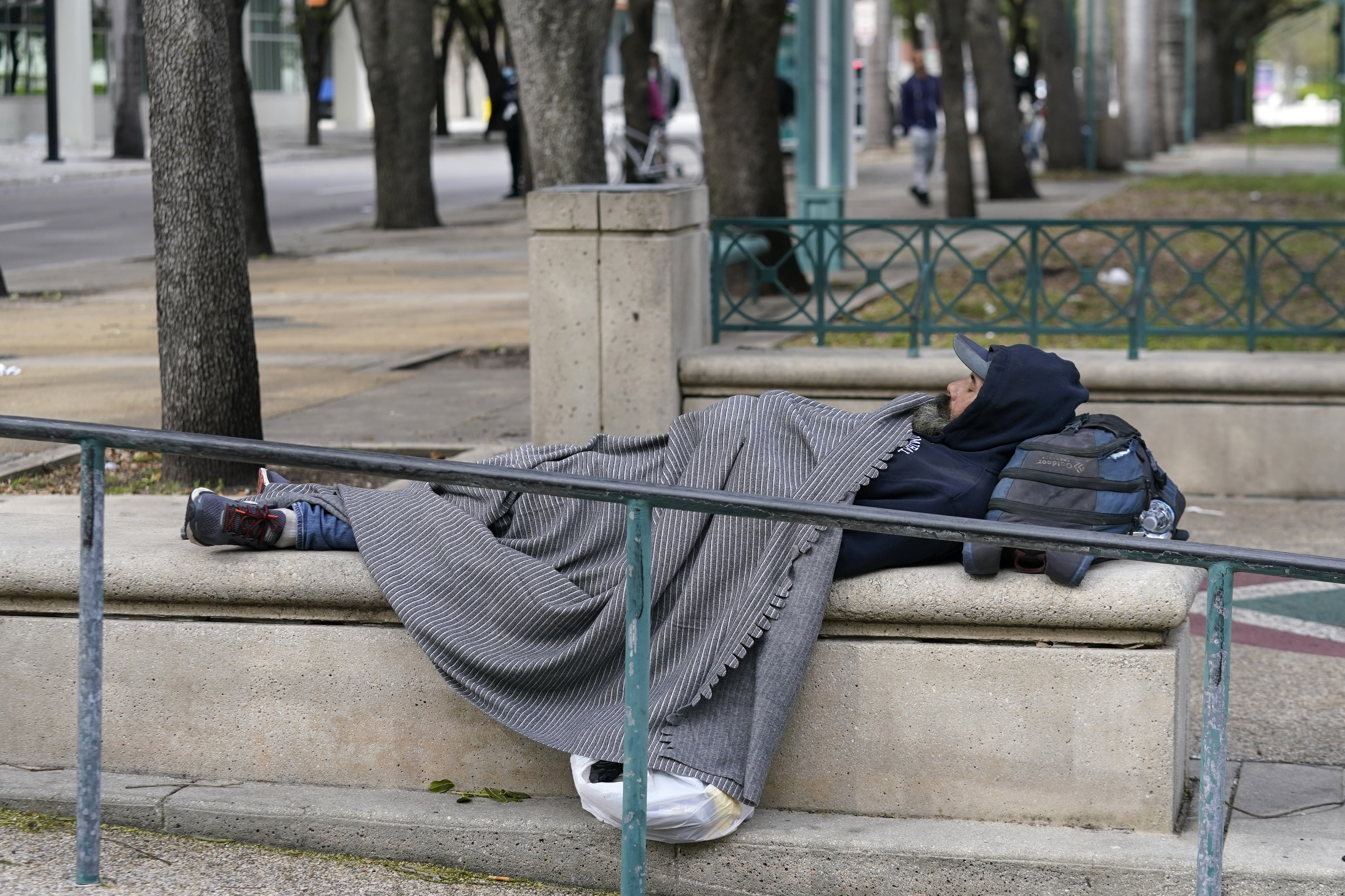 homeless man sleeps in Miami park with blanket over him, Jan. 22, 2022