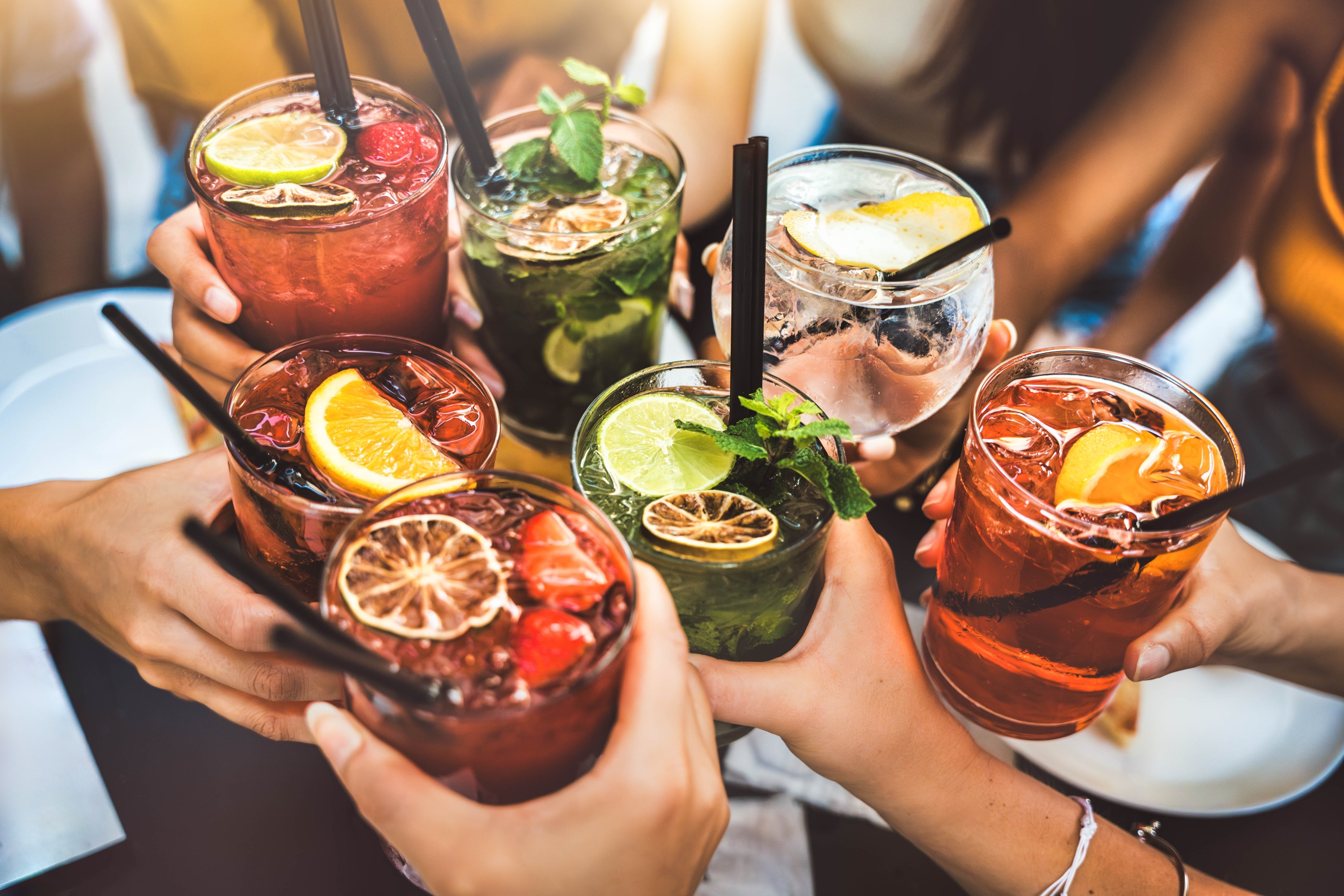 People toasting cocktail glasses at a bar.