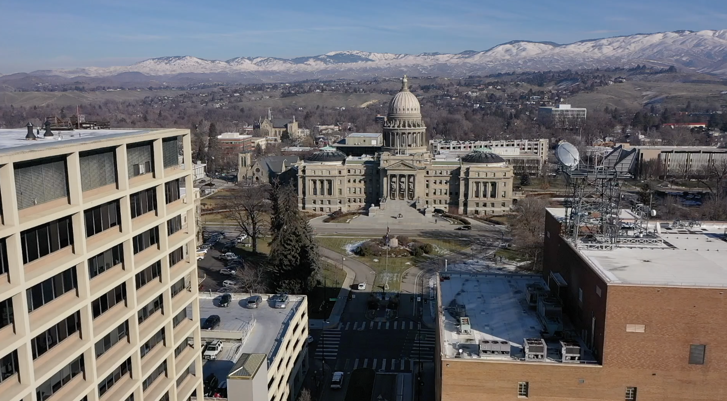Idaho State Capitol in Winter with snowy mountains and a blue sky behind it.