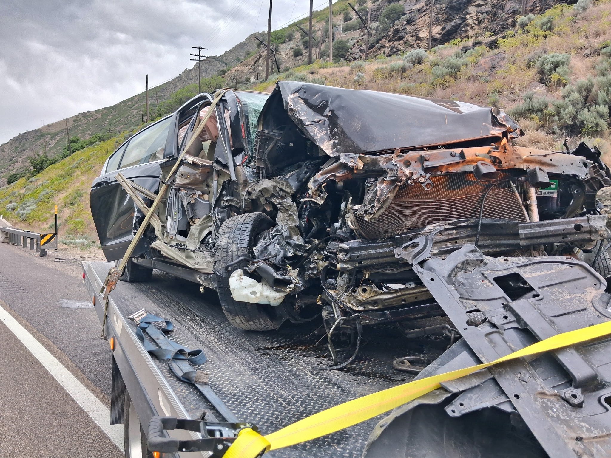 A photo from the crash scene released by Mountain Green Fire Protection District. A damaged SUV sits in the bed of a tow truck. The front is completely crumpled, with bits of the engine poking out.