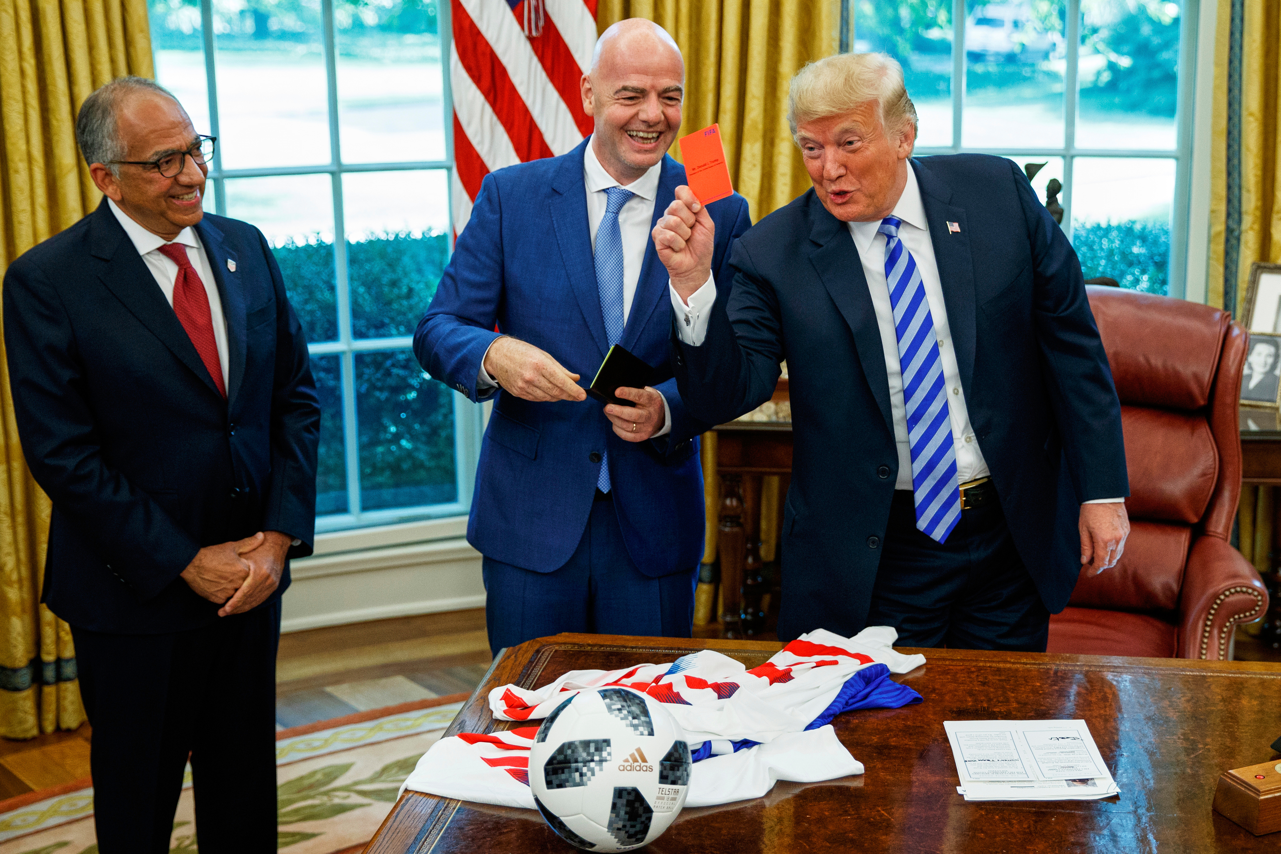 FILE - President Donald Trump holds up a red card during a meeting with FIFA president Gianni Infantino, center, and United States Soccer Federation president Carlos Cordeiro, left, in the Oval Office of the White House, Aug. 28, 2018, in Washington. 