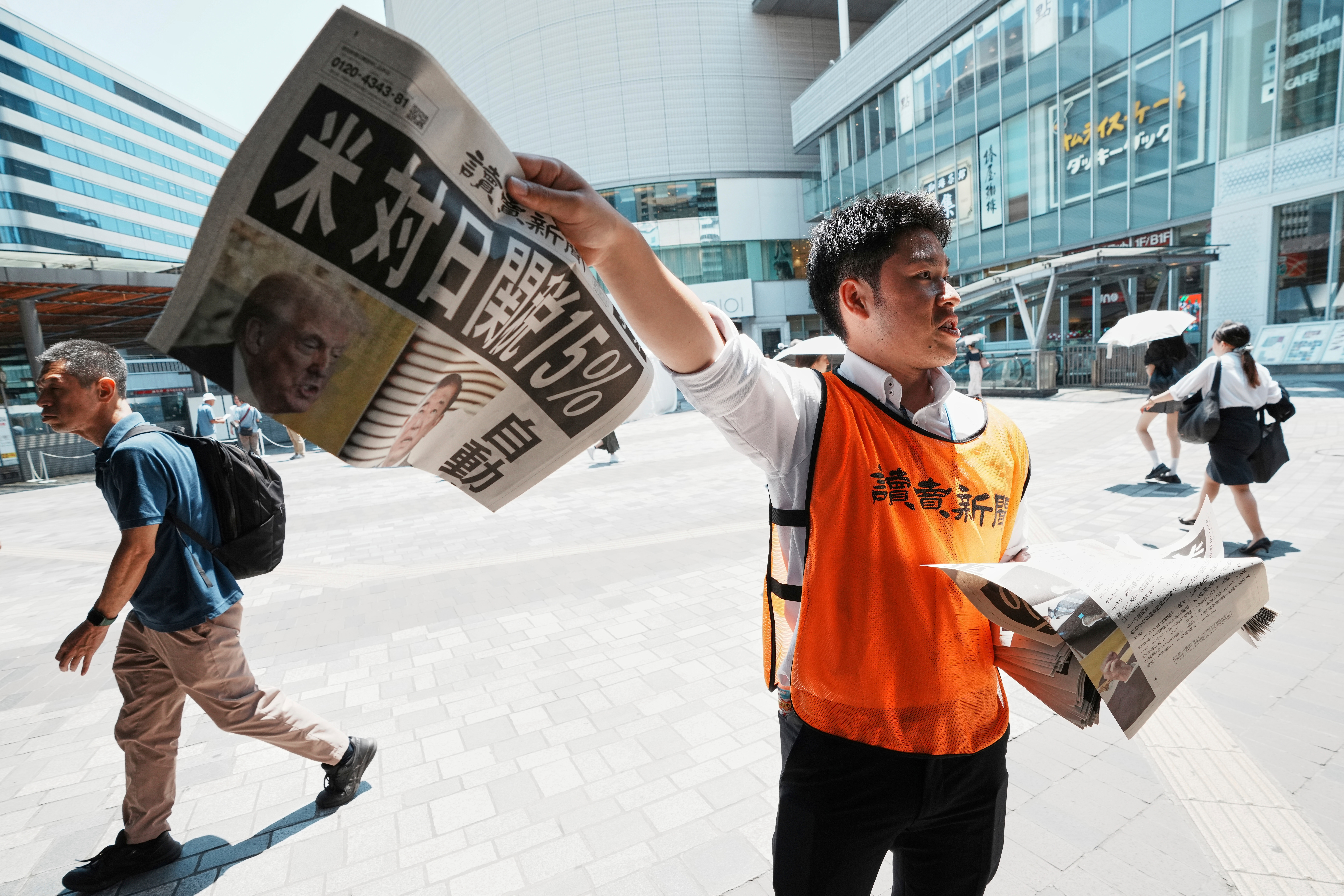 A staff member distributes an extra edition of the Yomiuri Shimbun newspaper reporting that President Donald Trump announced a trade framework with Japan on Tuesday, Wednesday, July 23, 2025, in Tokyo.  The headline reads "U.S.,  a 15% tax on goods imported from Japan."