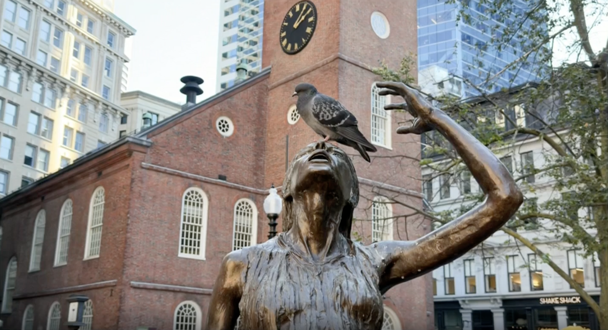 A bird resting on a statue of a woman in Boston.