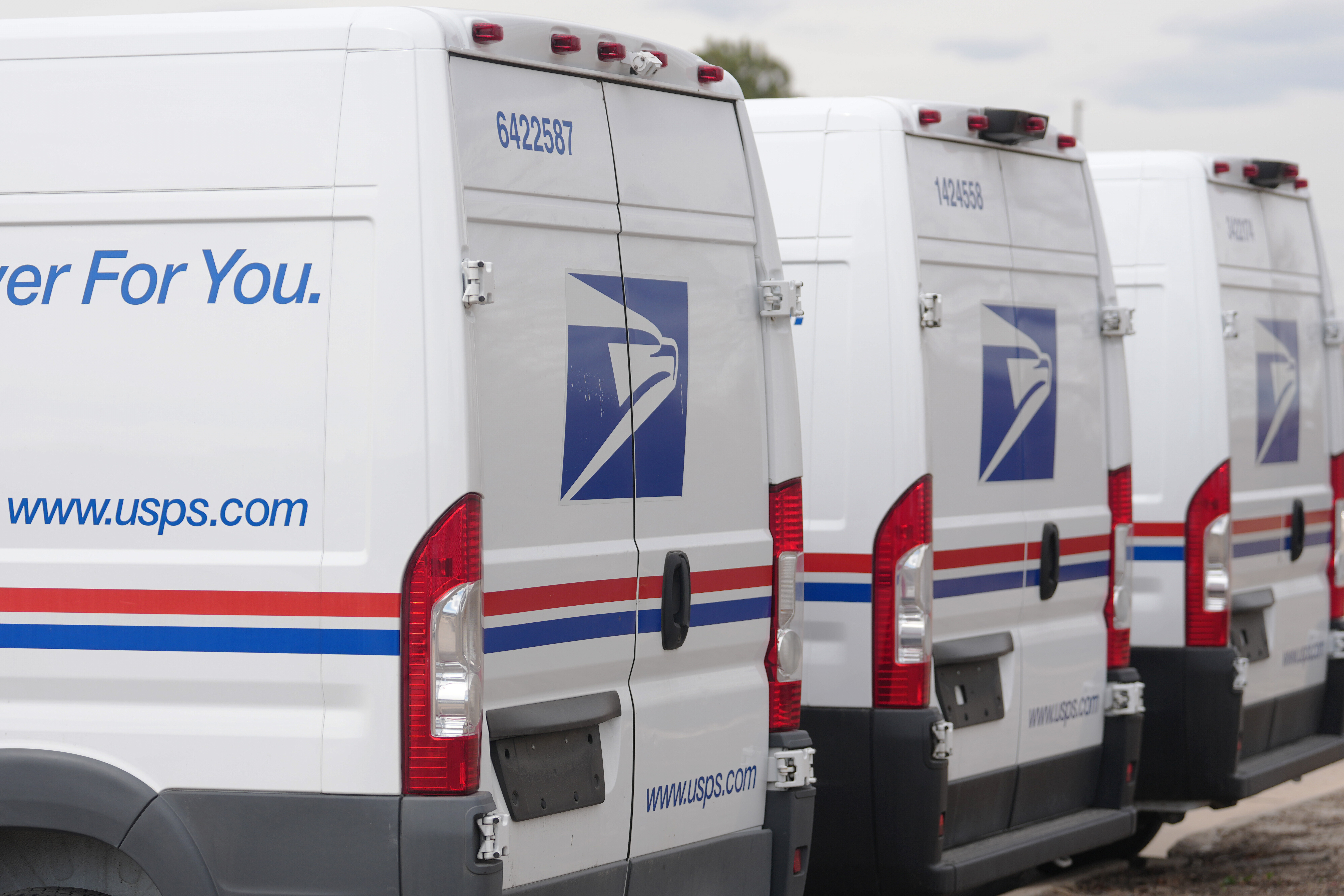 FILE - The United States Postal Service logo is shown on delivery vans parked outside the main post office March 23, 2026, in east Denver.