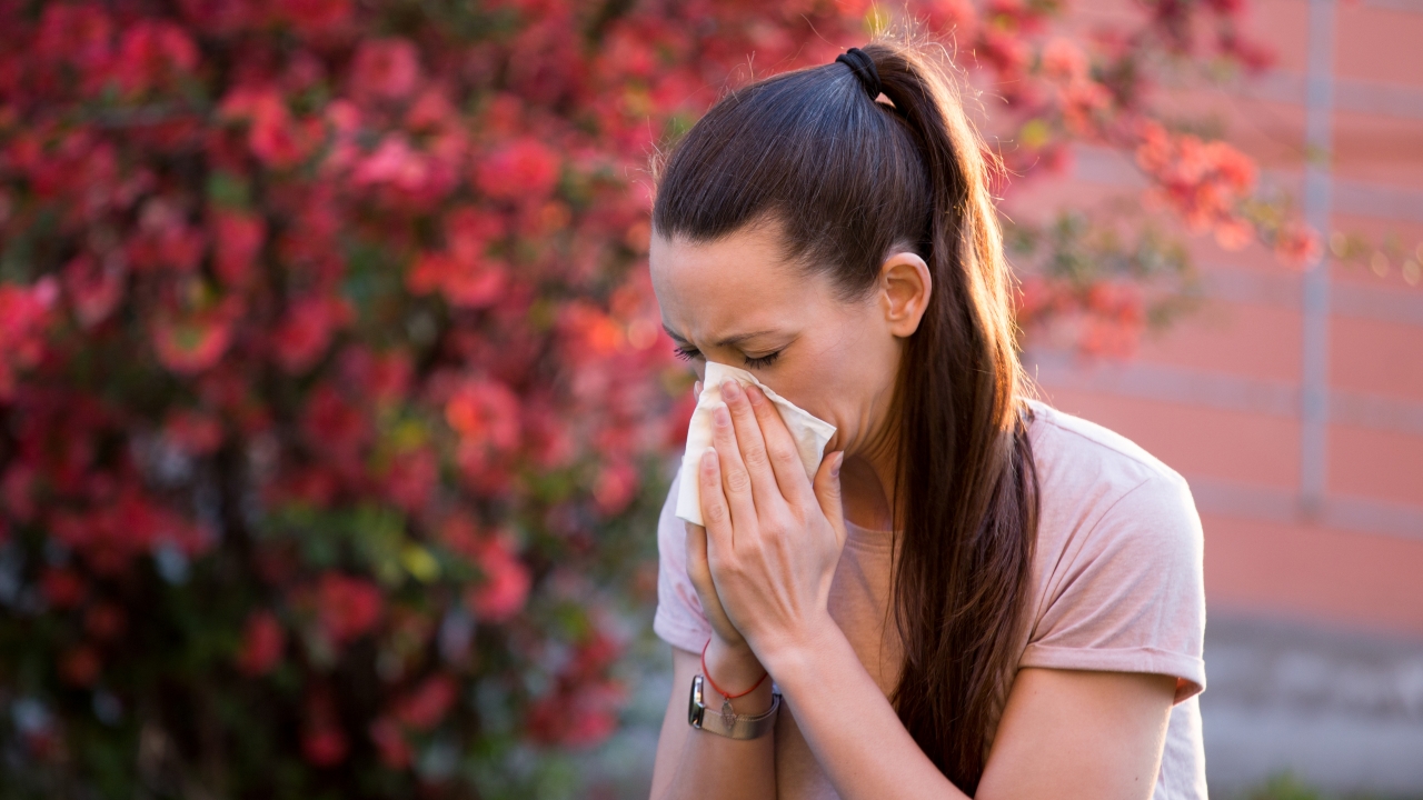 Woman sneezing in front of blooming tree.