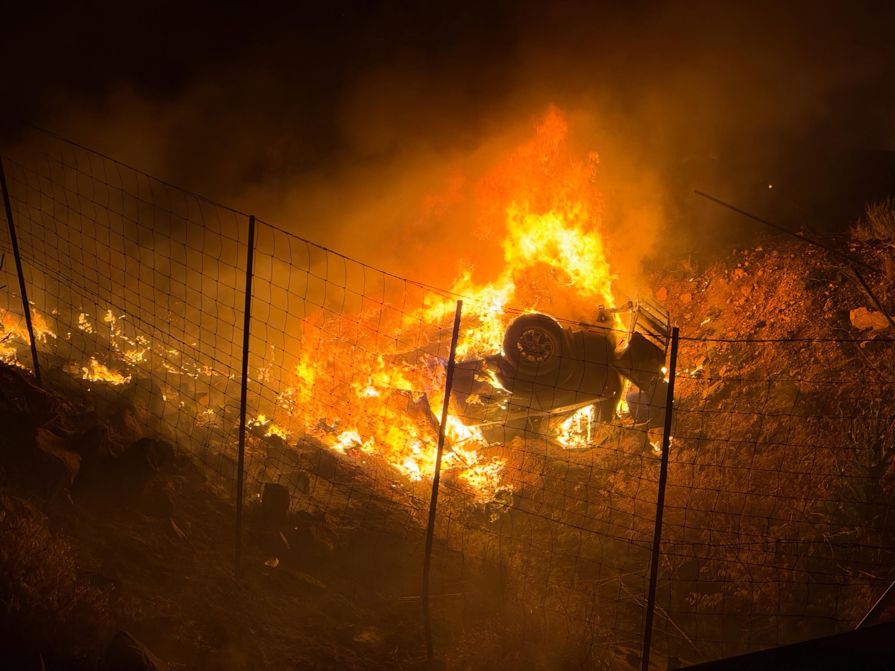 A photo from the scene released by Hurricane Valley Fire and Rescue. It's nighttime, and the overturned car burns, filling the scene with light from the flames.