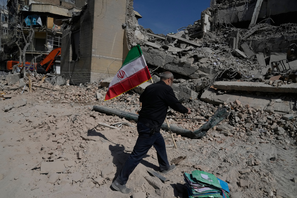 A man carries an Iranian flag to place on the rubble of a police facility struck during the U.S.–Israeli military campaign in Tehran, Iran, Wednesday, March 4, 2026.