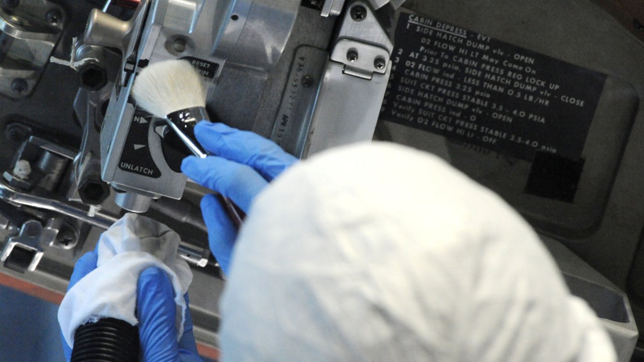 A brush and vacuum are used to clean the hatch of the Apollo 16 lunar spacecraft