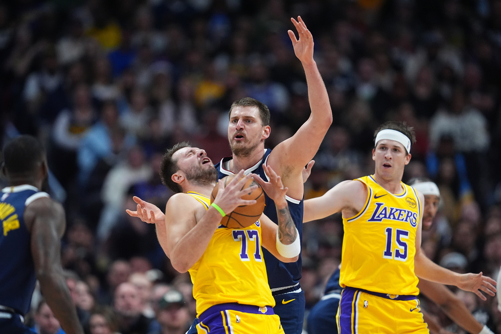 Los Angeles Lakers guard Luka Dončić, left, reacts after getting hit in the face by the ball while fighting for control with Denver Nuggets center Nikola Jokić as Los Angeles guard Austin Reaves, right, looks on in the first half of an NBA basketball game Thursday, March 5, 2026, in Denver.=